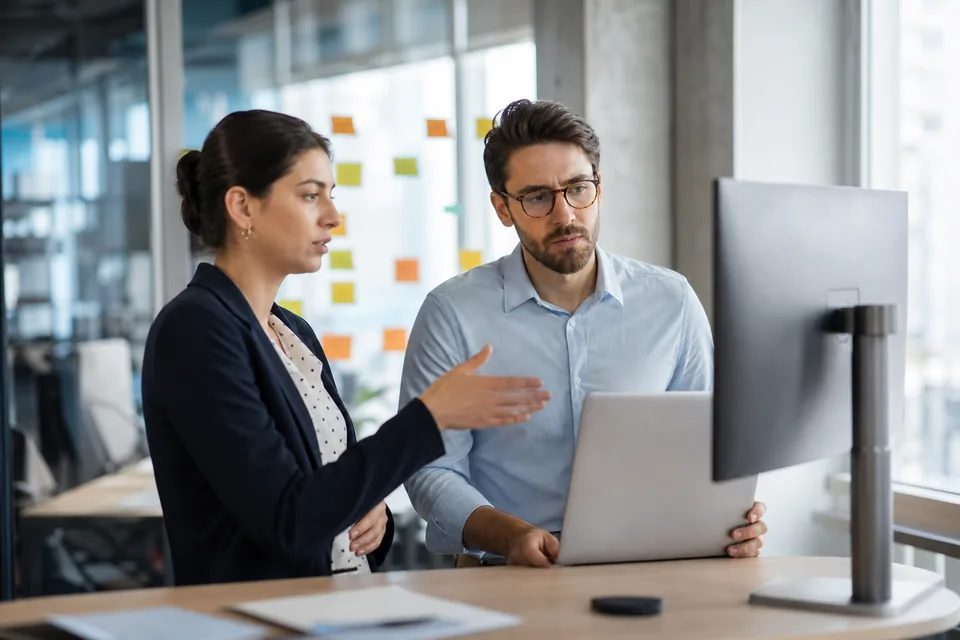 Sales manager and software engineer discussing a CRM workflow at a standing desk with sticky notes on a glass wall
